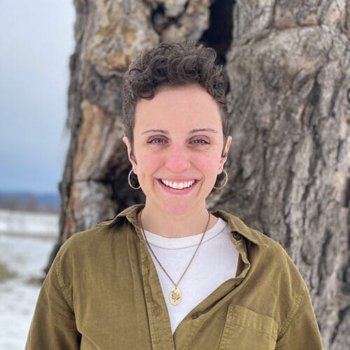 woman with short hair standing in front of wide tree - Rebecca Roman at Vermont Land Trust