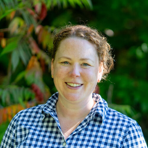 woman in blue-and-white checked shirt smiling at camera