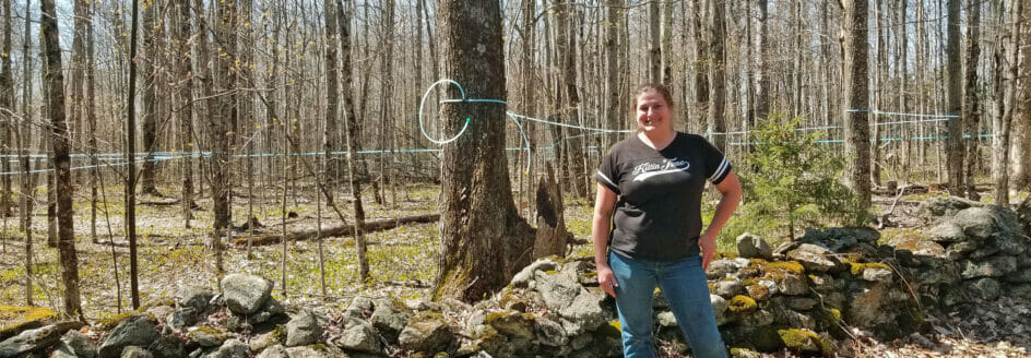 Jessica Boone of Hi Vue Farms standing by old stone wall on her conserved forestland in Vermont