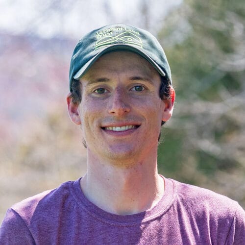 Young man wearing purple t-shirt and green baseball cap smiling at camera