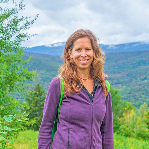 Woman in purple jacket at hill summit with distant hills in background