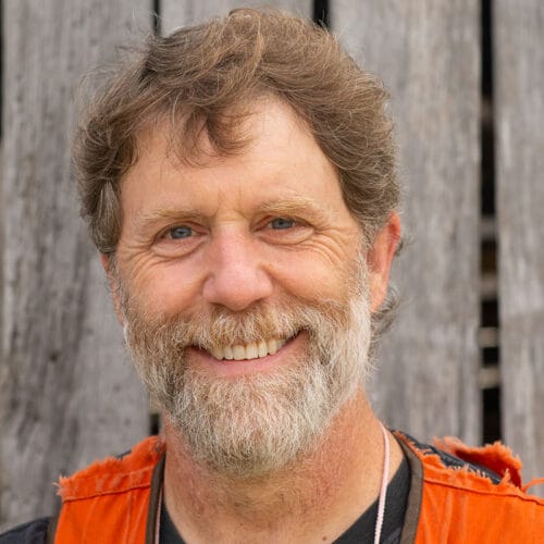 bearded man smiling at camera with gray barn wall behind