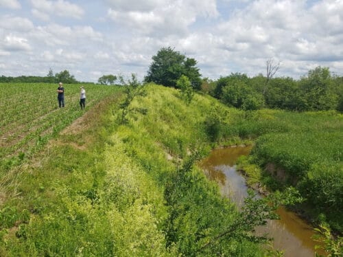 Two people stand in a farm field next to a small stream. Franklin County Vermont