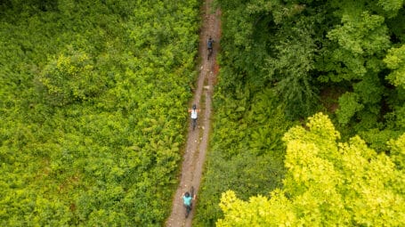 aerial shot of 3 bikers on recreation trail, with shrubs on left and trees on the right. Hinesburg Town Forest Vermont