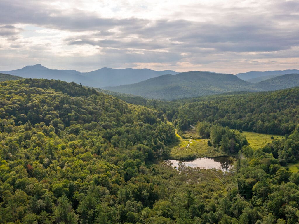 Aerial photo of forested hills on left with a pond and wetland at its base. Landscape of Hinesburg Town forest Vermont 