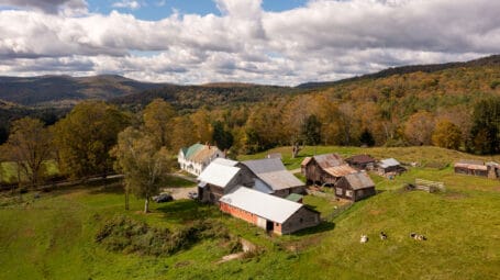 aerial of farmstead and hills with fall colors in distance. Vermont. King Farm