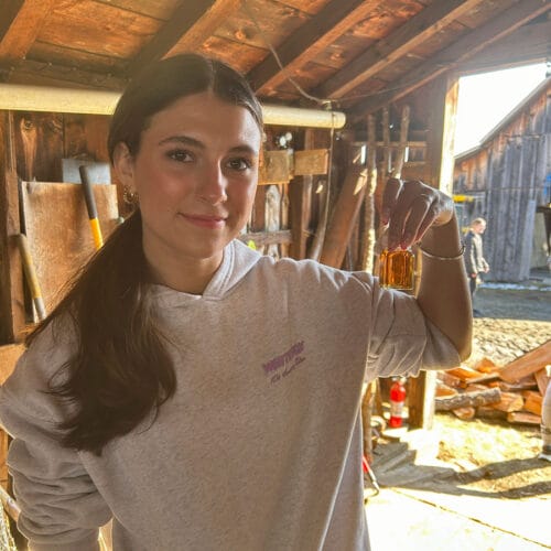 Young woman holding up a small glass jar with maple syrup. King Farm Vermont