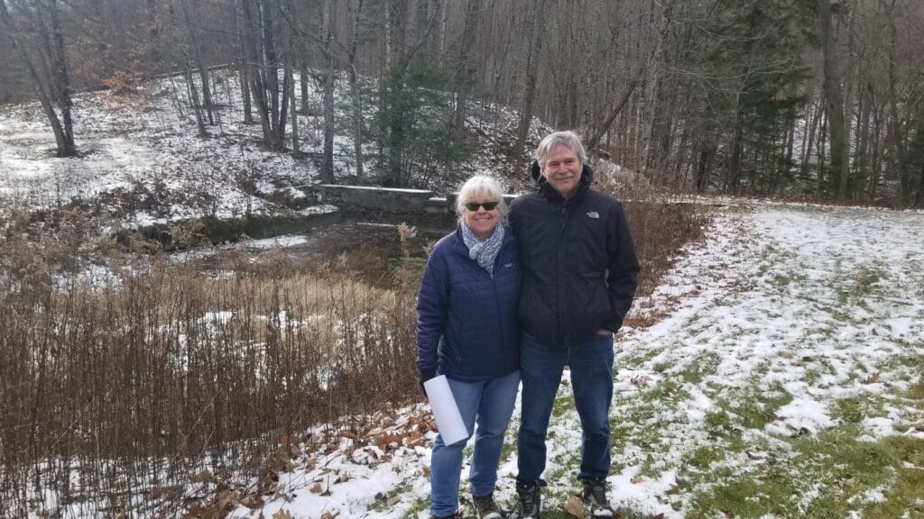 Man and woman smiling in front of snow and ice-covered dam