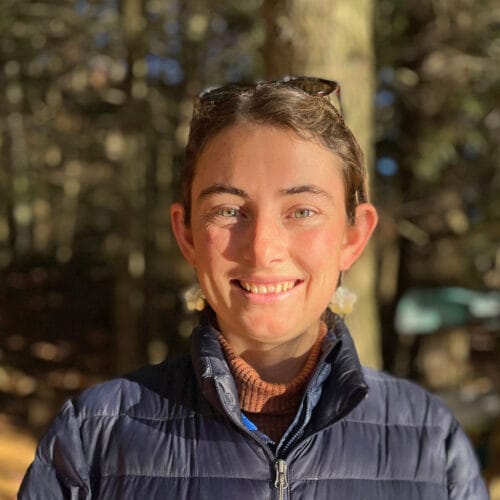 young woman smiling at camera with fall woods behind. Vermont