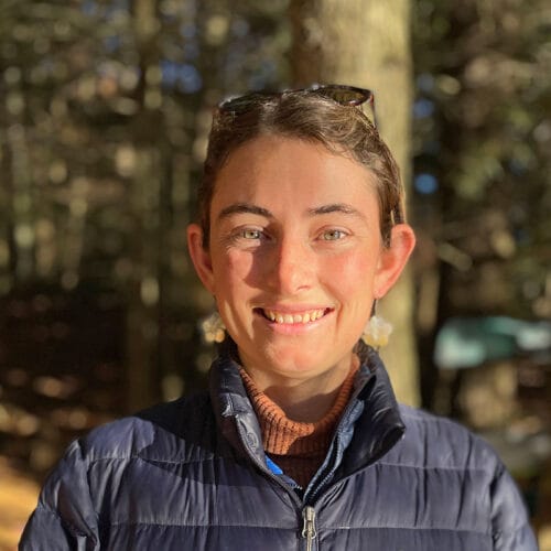 young woman smiling at camera with fall woods behind. Vermont