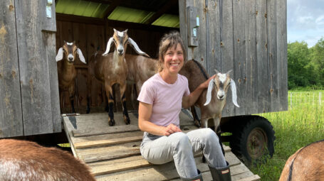 woman smiling at camera, seated on ramp for mobile farm shed with goats. Bennington Vermont