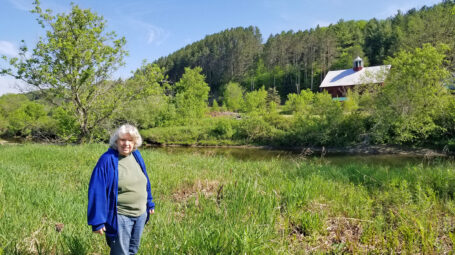 woman standing in pasture with a river flowing behind and a barn beyond. Lamoille River Vermont