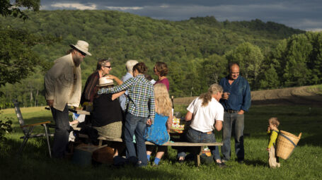 A family gather outside around a picnic table on a sunny evening