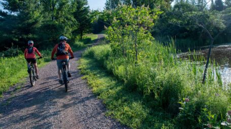 Two bikers on a gravel road with a pond on the right