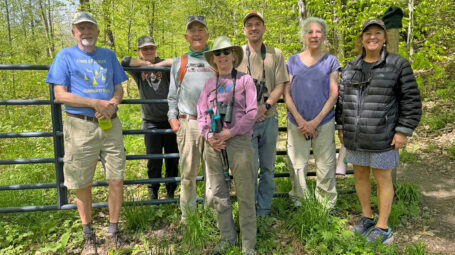 group of men and women smiling at camera and standing at entrance to wooded area with trails. Berlin town forest addition. Vermont