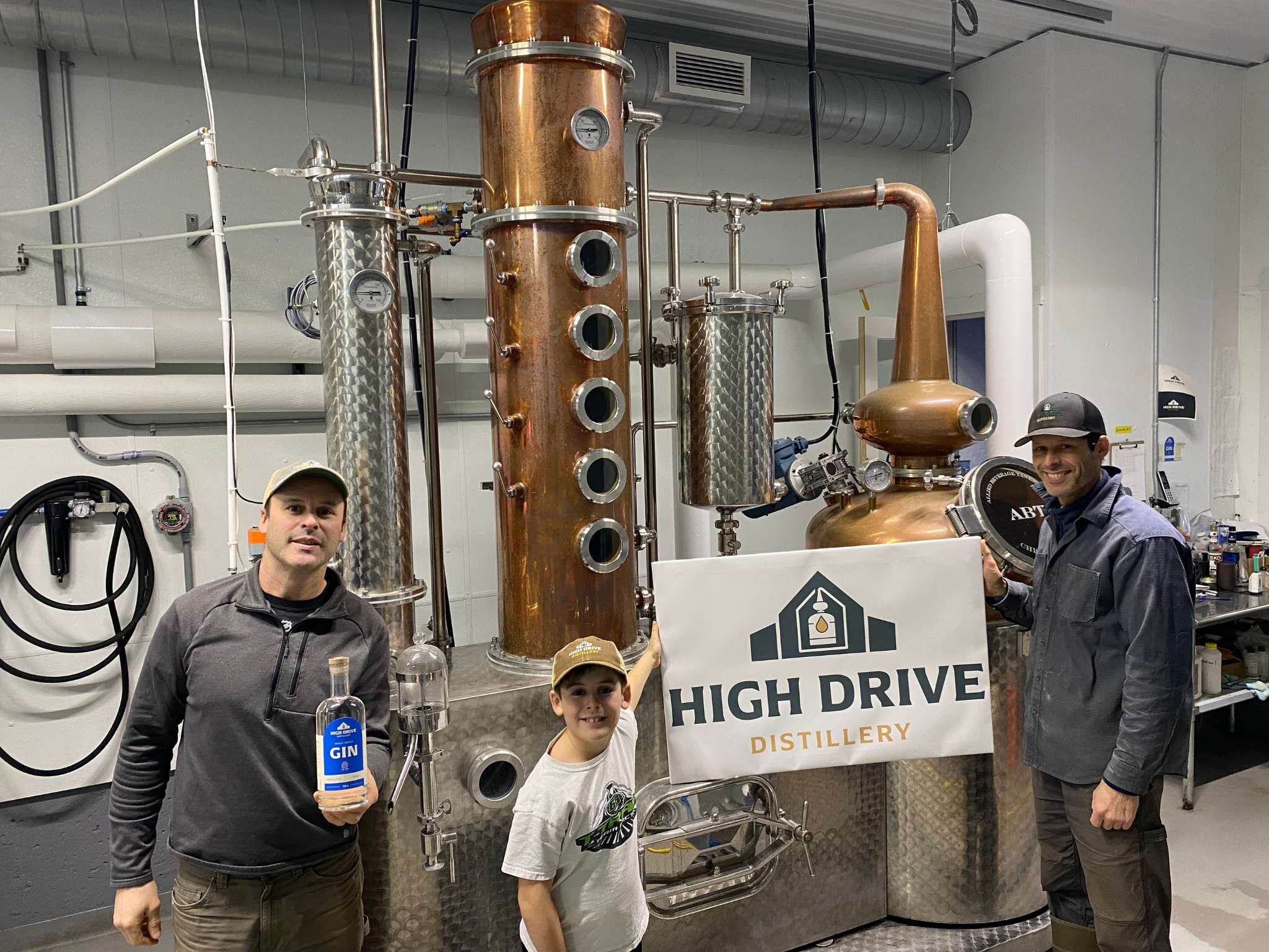 Two men and a boy stand in front of a still holding a sign that reads "High Drive"