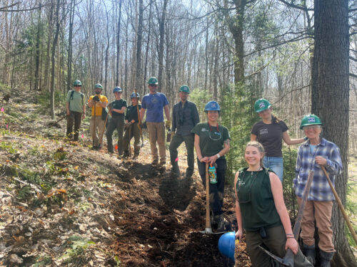 VYCC crew and VLT staff gather to build a trail in a leaf-covered forest clearing.