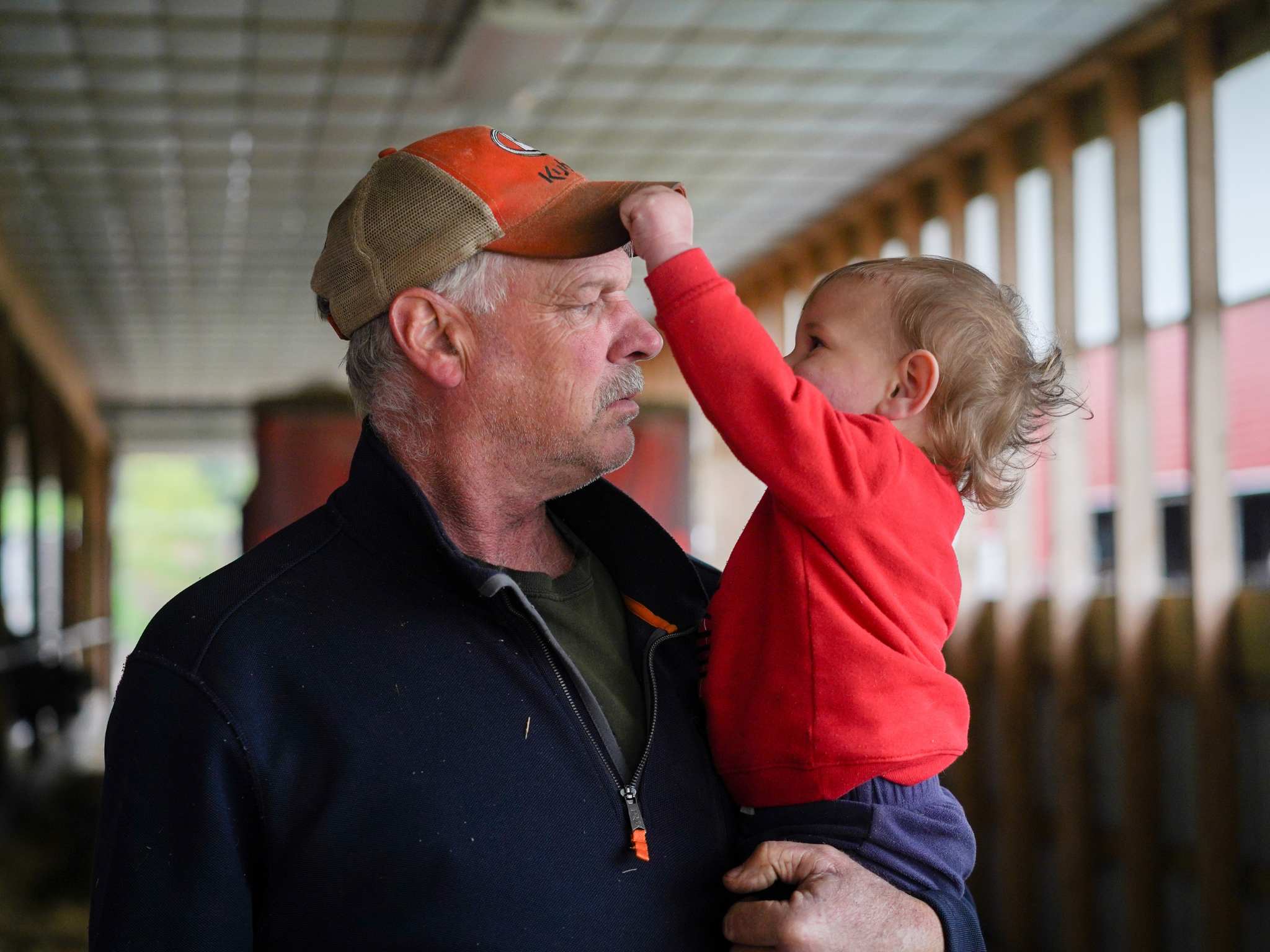 An older man holds a toddler, who grabs the brim of his hat