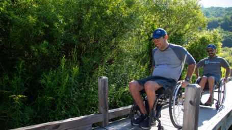 two men in wheelchairs on a boardwalk. summer.
