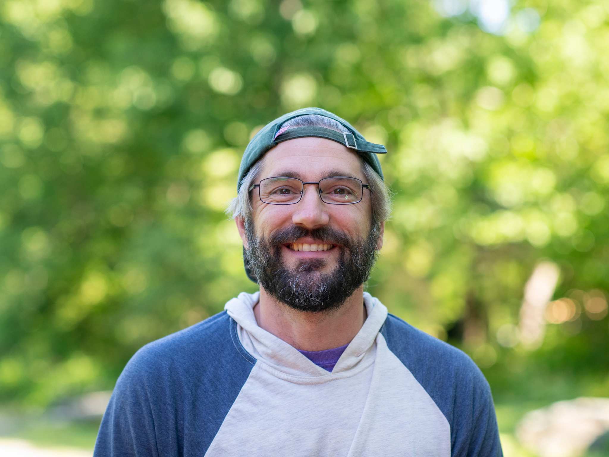 A bearded white man wearing a hat smiles at the camera