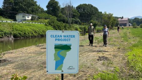 A sign reads "Clean Water Project" with two people behind.