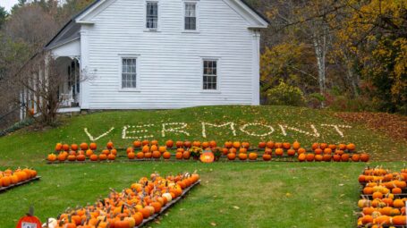 A white farmhouse with pumpkins arrayed in front, some spelling out "VERMONT."