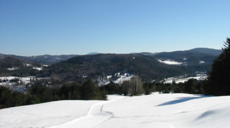 A smoothed path leads through a snow-covered field with a wide valley below.