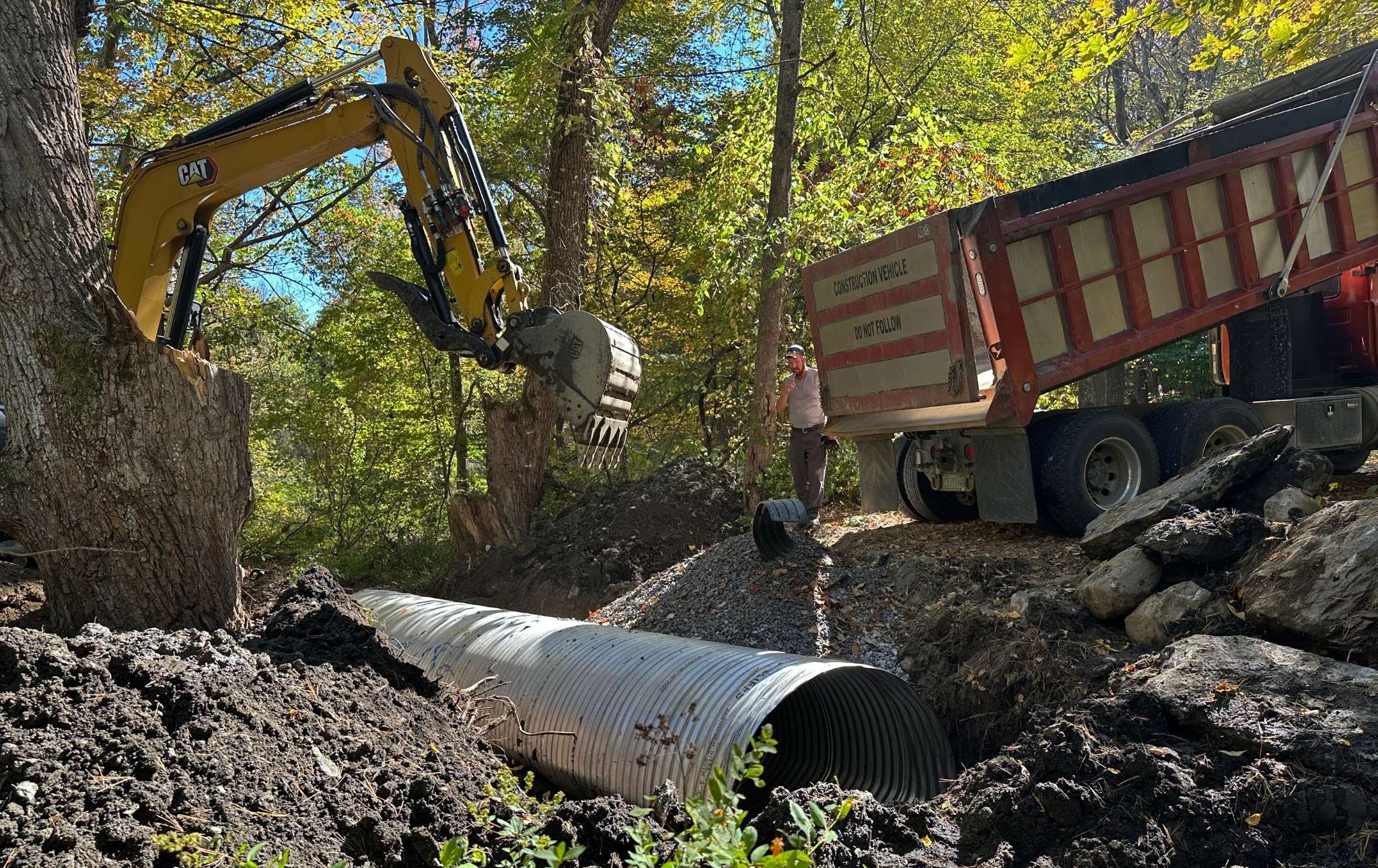 An excavator and dump truck install a new culvert in the stream.