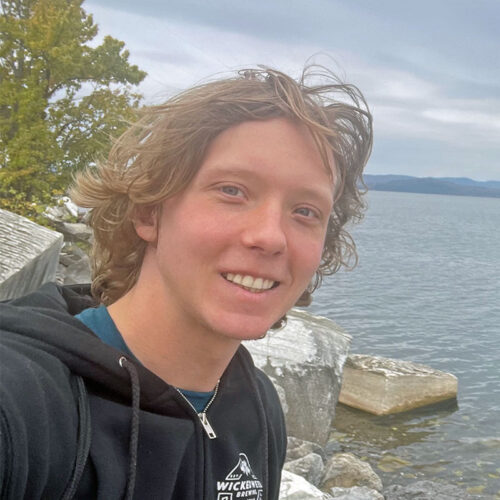 Young man at rocky shoreline with large lake beyond