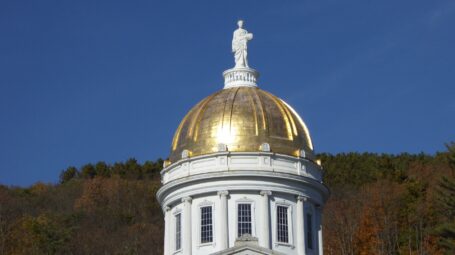 The Vermont State House golden dome, with trees and blue sky in the background