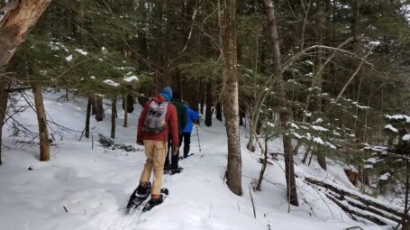 Three people snowshoe throught he snow woods att he Krusch Nature Preserve