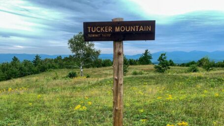 A sign that reads Tucker Mountain Summit 1690" with a green meadow in the background.