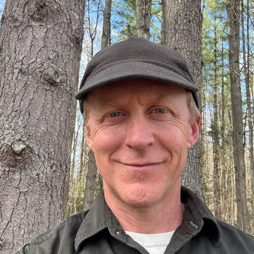 close up of man wearing hat standing in spring-time woodland