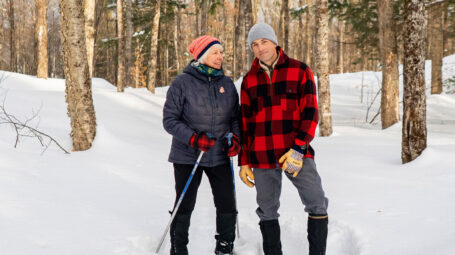 A woman and a man pause on a winter hike through snowy woods with glowing birches and evergreens around. Woodbury Vermont
