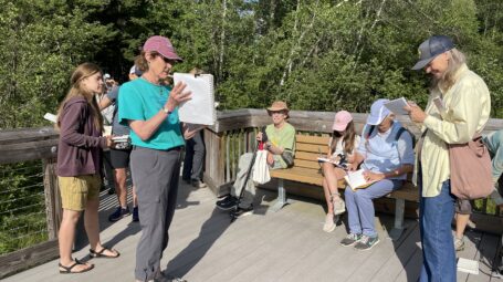 A group of people sit outdoors on a deck, journaling.