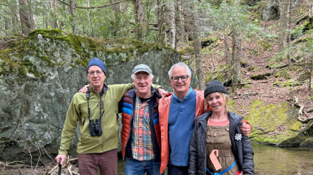 Four people in a forest with a large rock and a stream behind them. Waterbury Vermont