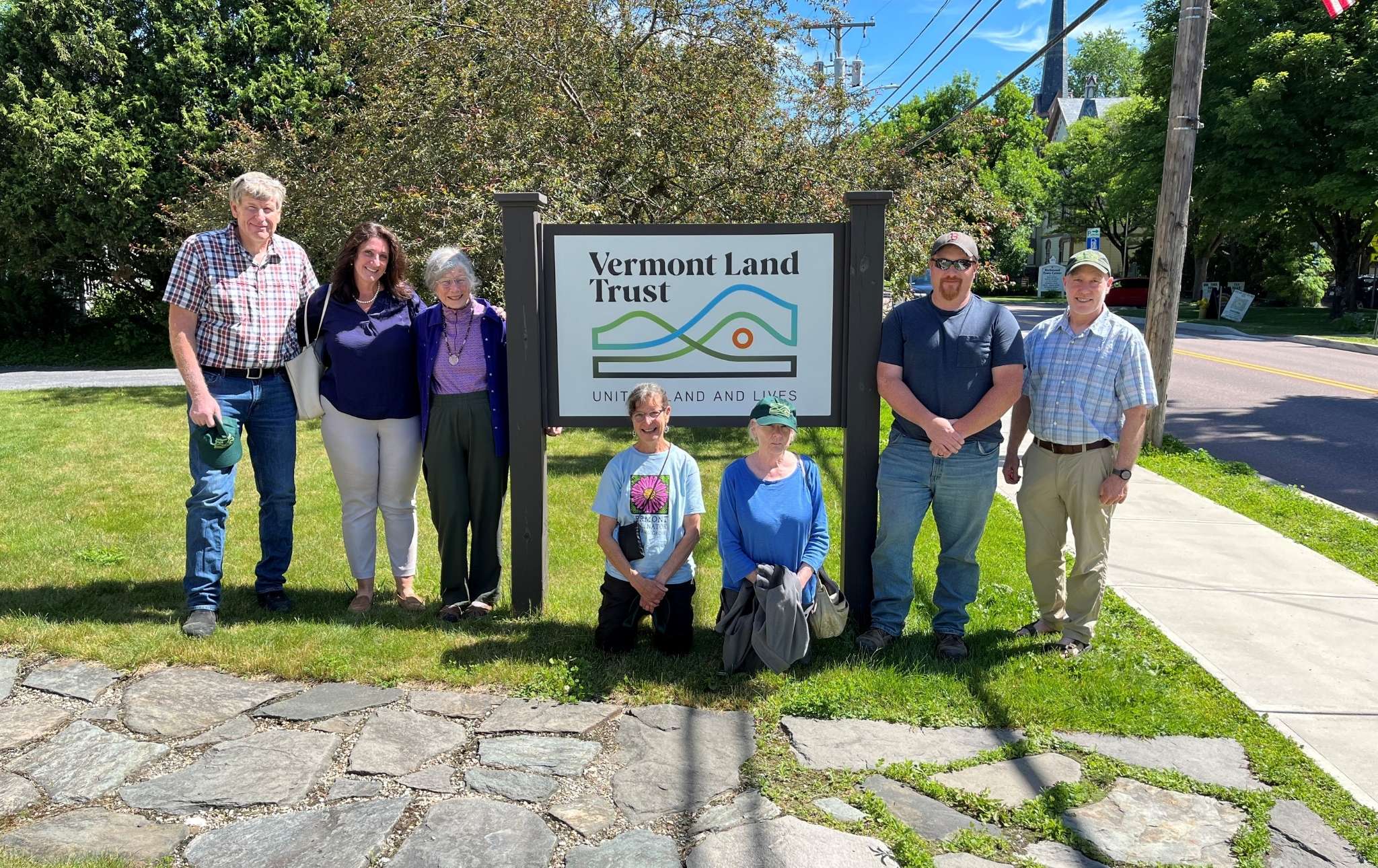 Seven people stand around a sign that says Vermont Land Trust.