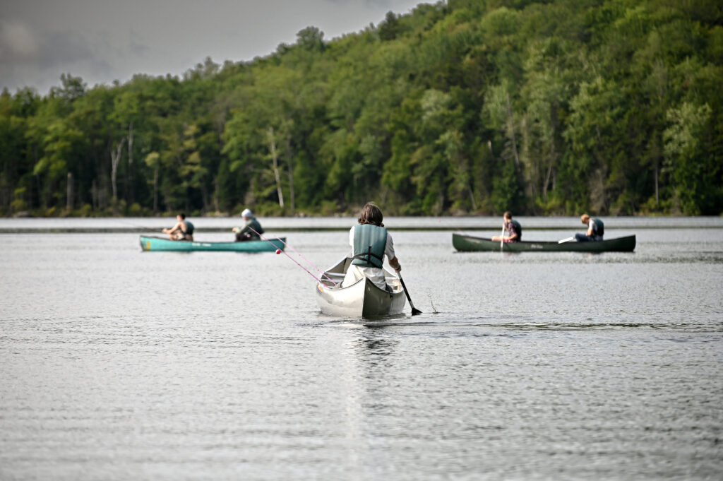 View from behind of campers canoeing on a lake, looking beyond at a forested hill.