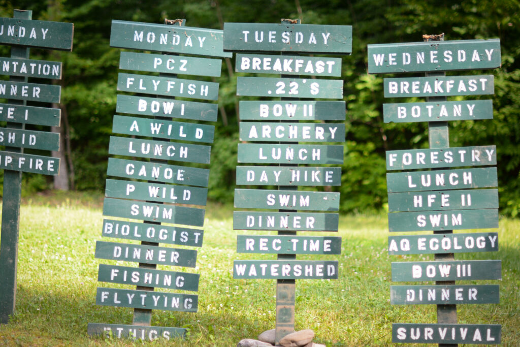 Green signs on wooden posts with camp activities listed.