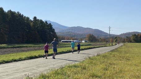 5K participants run along a farm road, with mountains in the background.
