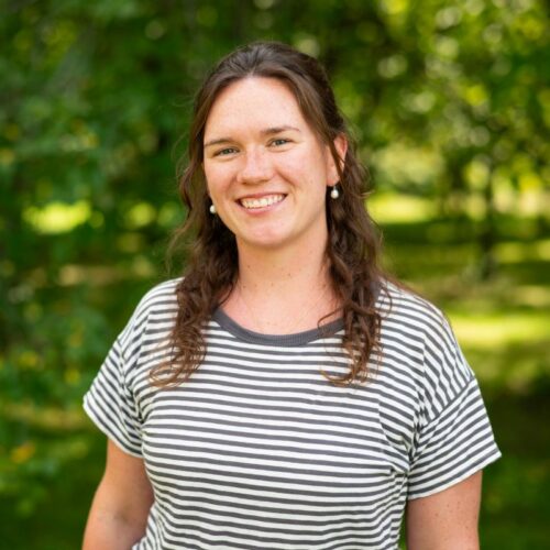 A smiling white woman with greenery behind her