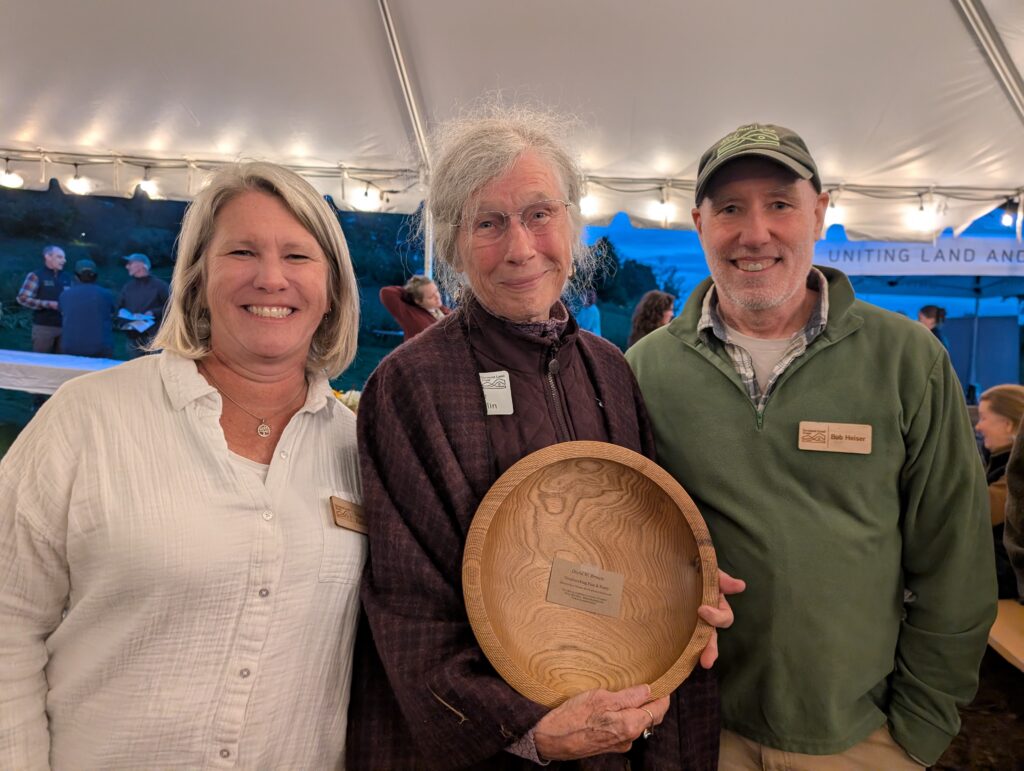 Three people smiling, the center one holding a gifted wooden bowl.