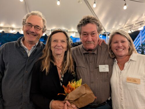 Four people smiling, one holding flowers.