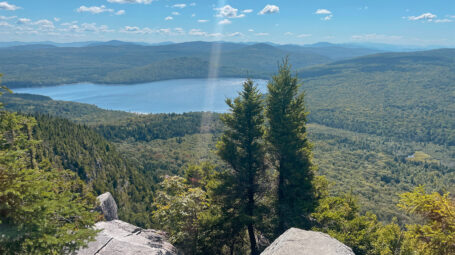 photo on sunny day at clifftop summit with view forested mountains and large lake. Vermont, northeast Kingdom